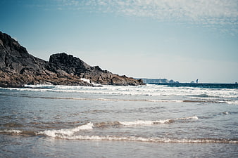 Rugged rocky coastline with ocean waves and distant sailboat