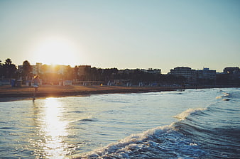Woman jogging on beach at sunrise with city skyline