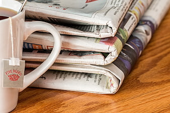 Stack of folded newspapers with tea cup on wooden table