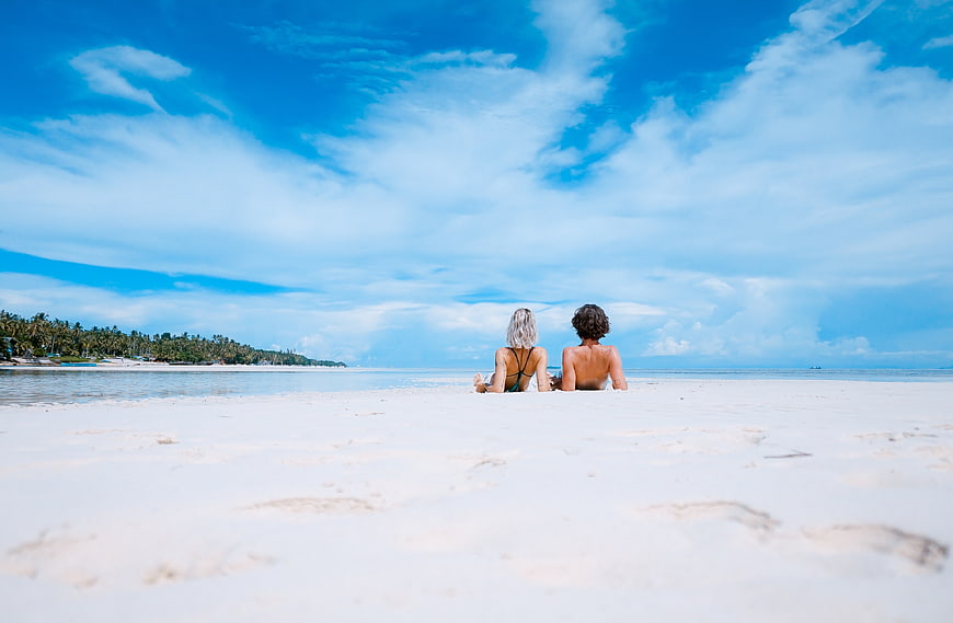 Couple relaxing on white sand beach under blue sky