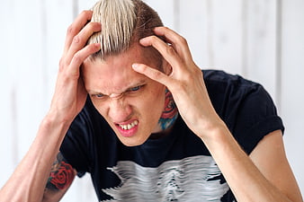 Young man with platinum hair holding head in pain