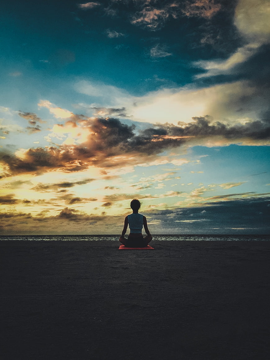 Woman meditating on beach at sunset