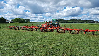 Green tractor with red hay rake in field