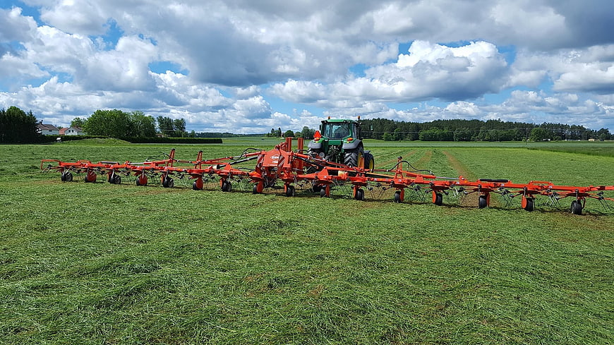 Green tractor with red hay rake in field