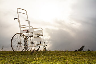 Old wheelchair on grassy hill under dramatic cloudy sky