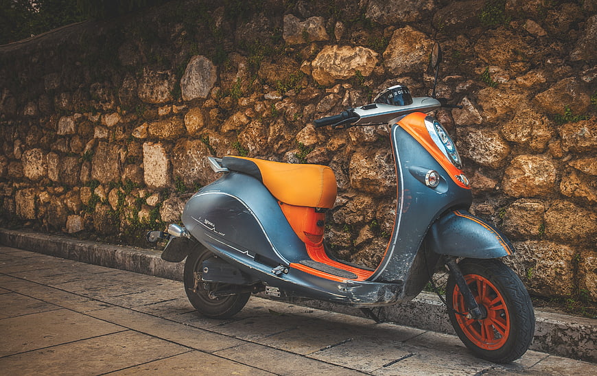 Vintage Blue and Orange Scooter Parked Against Stone Wall