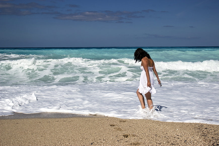 Woman in White Dress Walking in Ocean Waves on Sandy Beach
