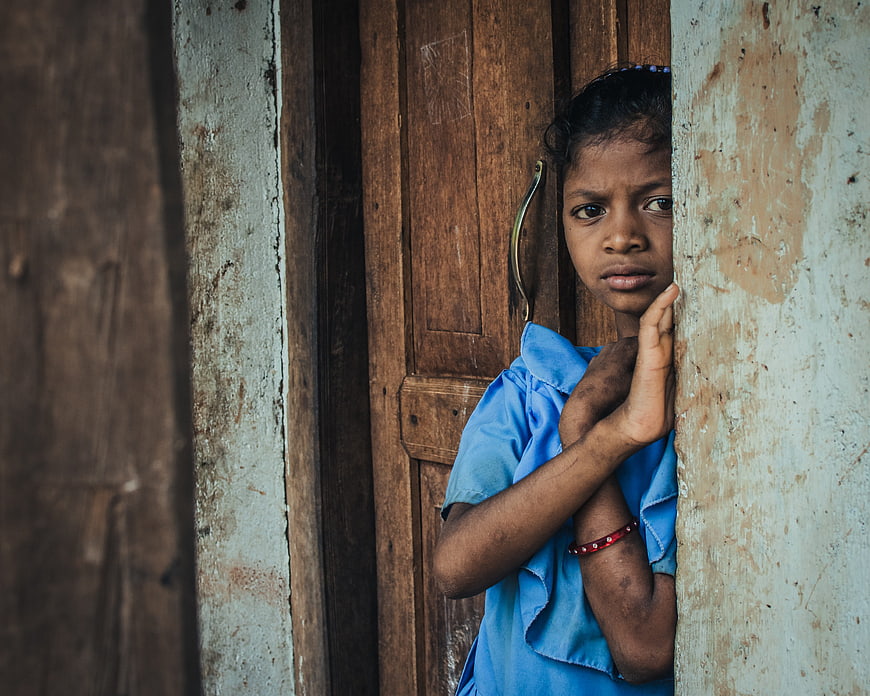 Portrait of a young Indian girl peeking from a weathered doorway