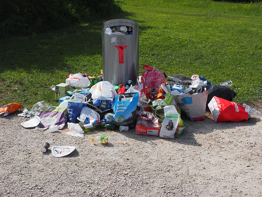Overflowing trash bin with scattered garbage on gravel path