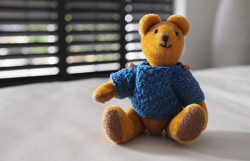 Cute Teddy Bear in Blue Knitted Sweater on White Surface