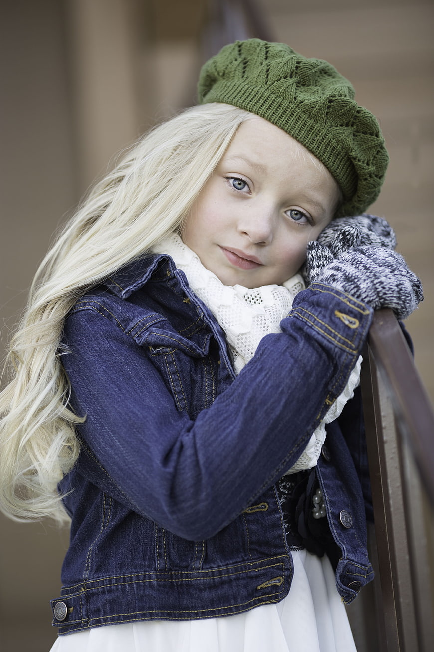 Portrait of a young blonde girl wearing a green knit hat and denim jacket