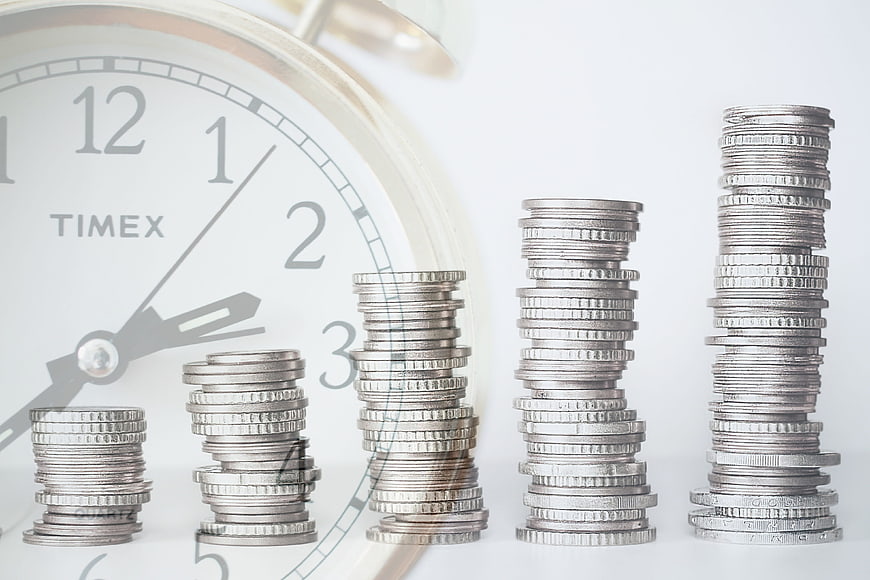 Ascending coin stacks in front of a Timex clock face