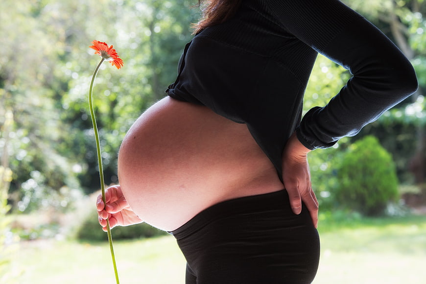 Pregnant woman holding orange flower in garden