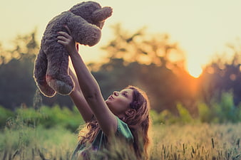 Woman holding teddy bear in field at sunset