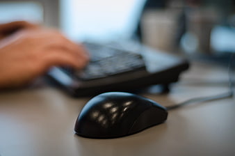 Black computer mouse on desk with blurred typing hands