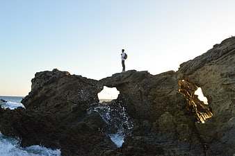 Man standing on coastal rock arch at sunset