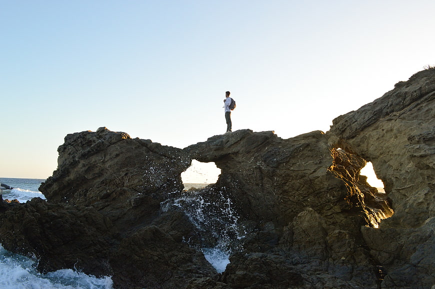 Man standing on coastal rock arch at sunset