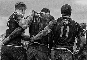 Muddy Rugby Players Huddling Together in Black and White