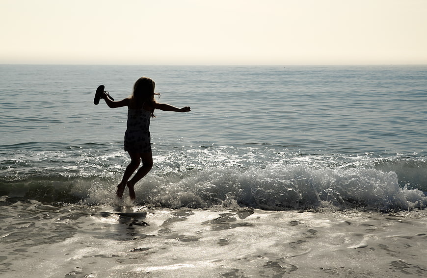 Girl jumping in ocean waves at sunset beach