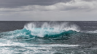 Powerful turquoise ocean wave crashing under cloudy sky