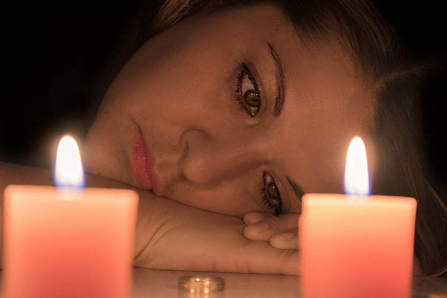 Sad woman face resting on hand between two lit candles