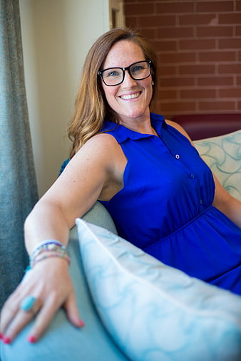Smiling woman with glasses in blue dress sitting on sofa