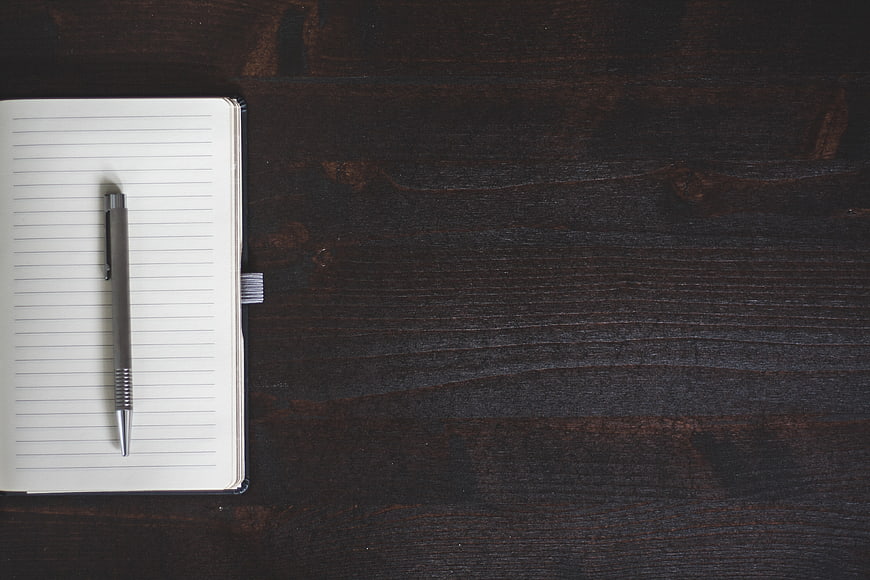 Minimalist notebook and pen on dark wooden desk background