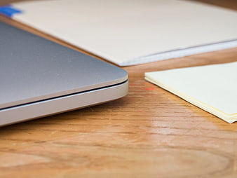 Close-up of laptop corner and notebook on wooden desk
