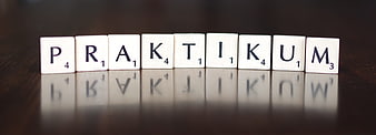 Scrabble tiles spelling the word Praktikum on a dark reflective surface