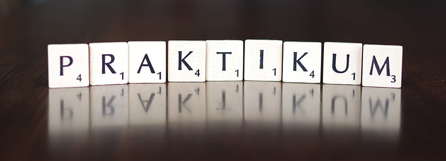 Scrabble tiles spelling the word Praktikum on a dark reflective surface
