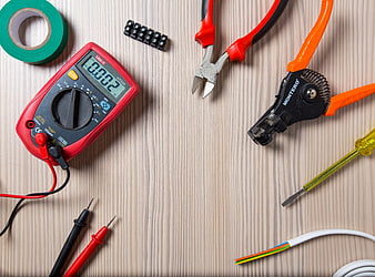 Electrician tools and multimeter on wooden workbench
