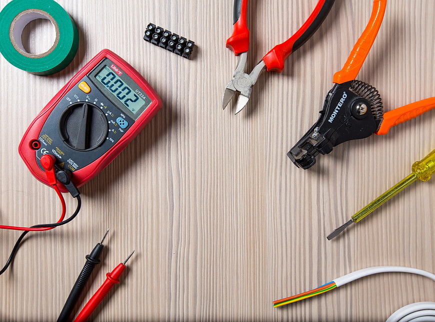 Electrician tools and multimeter on wooden workbench