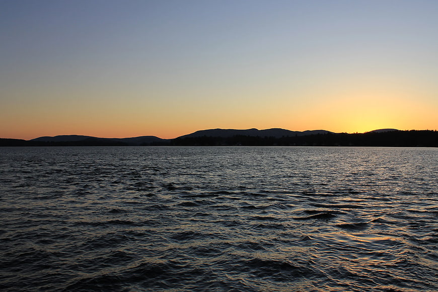 Sunset over Lake with Silhouetted Mountains and Rippling Water