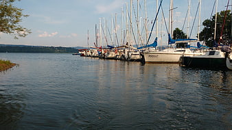 Sailboats docked in a calm lake harbor with blue sails