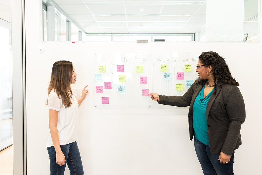 Two women discussing project on whiteboard with sticky notes