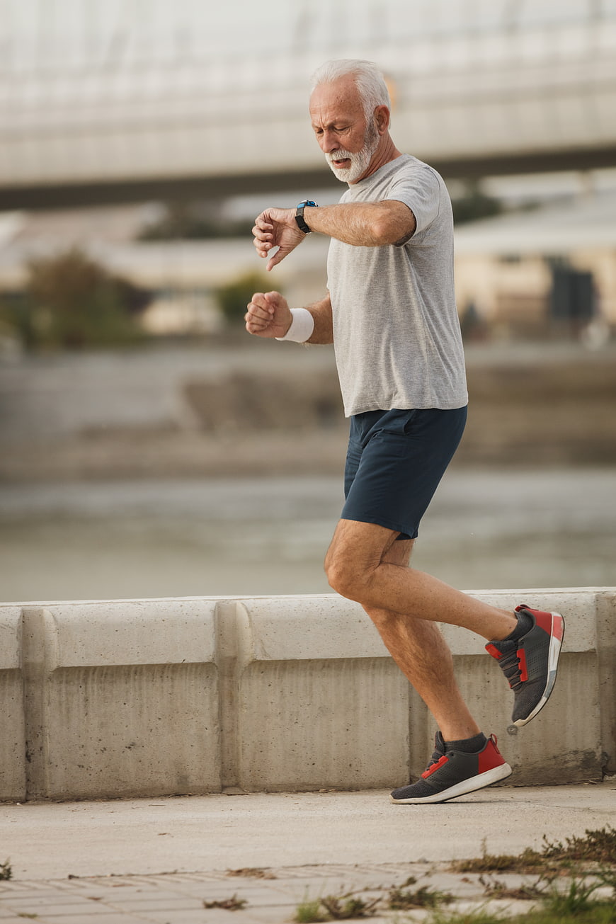 Senior man jogging outdoors checking smartwatch fitness tracker