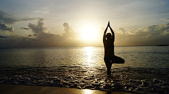 Silhouette of a man practicing yoga tree pose on a beach at sunset