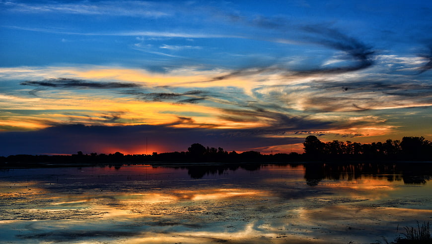Dramatic Sunset Reflection Over Calm Lake With Silhouette