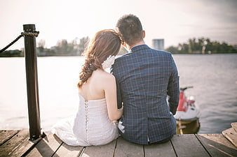 Bride and Groom Sitting on Wooden Dock by Lake