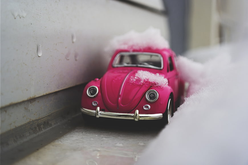 Pink toy car covered in snow on a windowsill