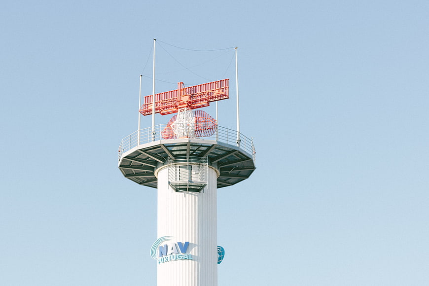 White Radar Tower with Red Antenna Against Blue Sky