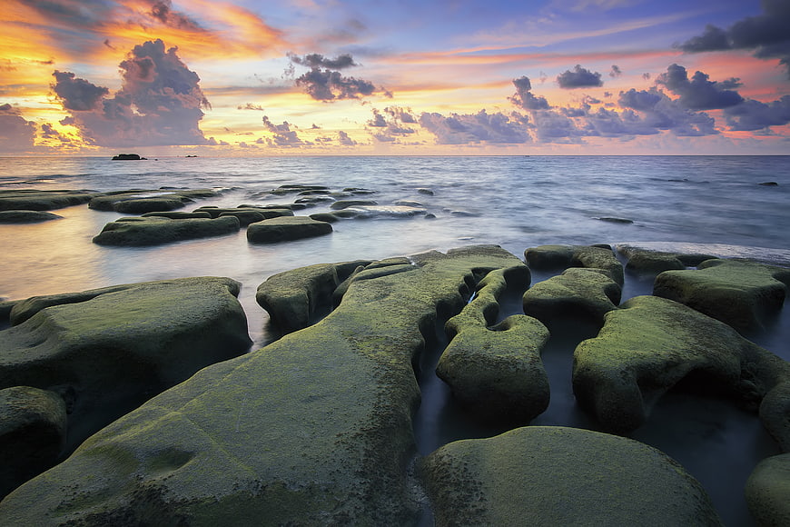 Dramatic Sunset Over Mossy Coastal Rocks and Ocean