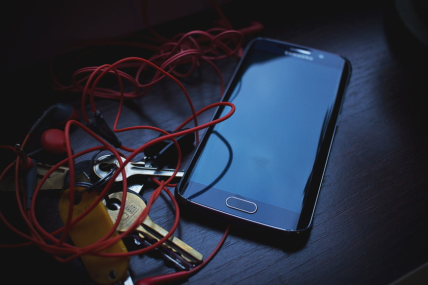 Smartphone with red earphones and keys on dark wood