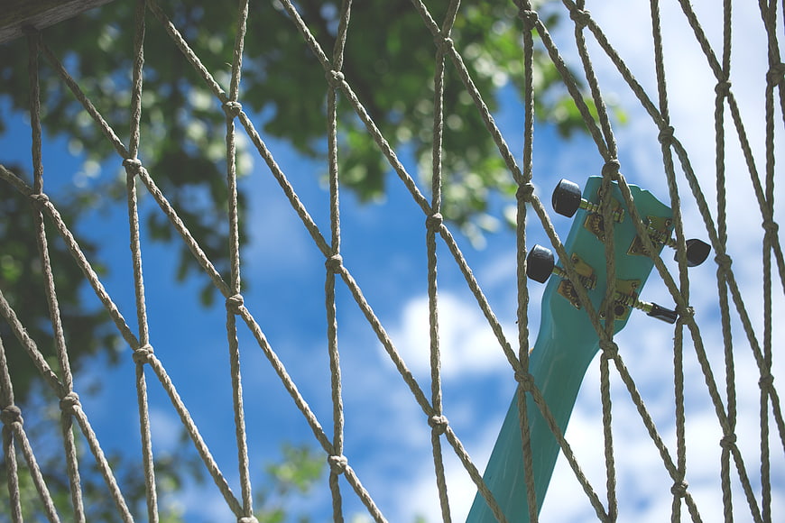 Teal guitar headstock behind rope netting against blue sky
