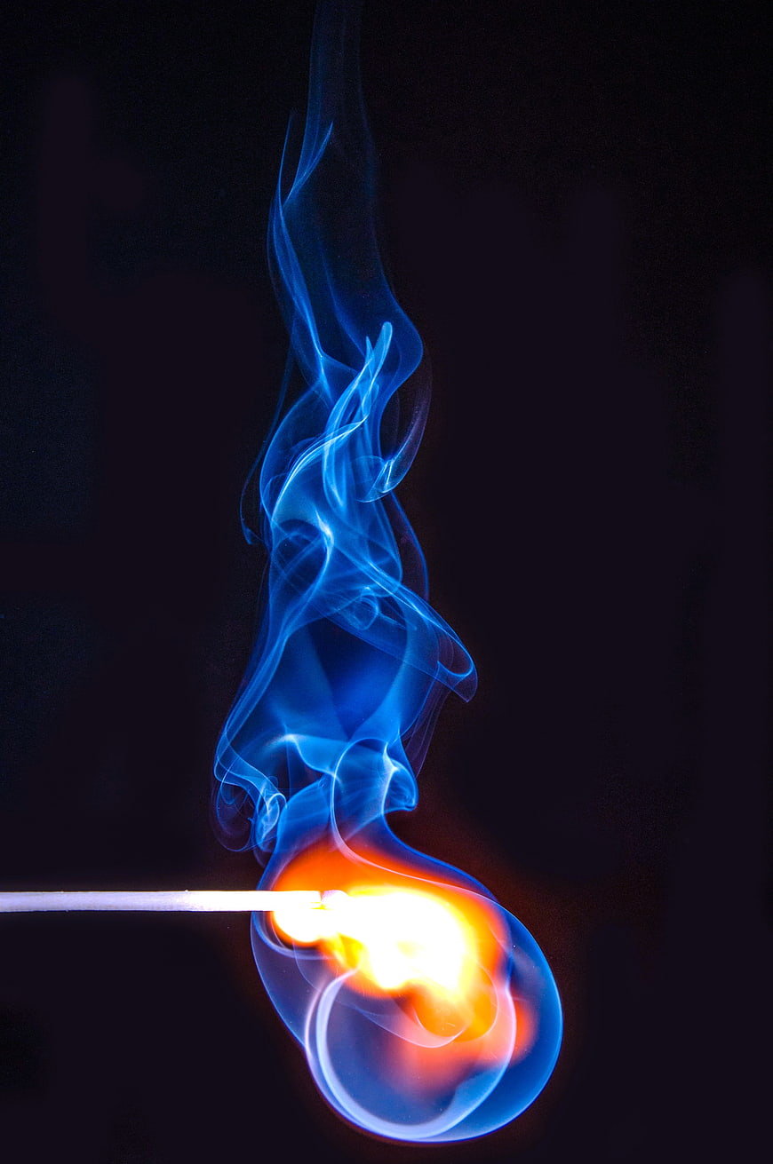 Blue Flame and Smoke Rising from a Lit Match on Black Background