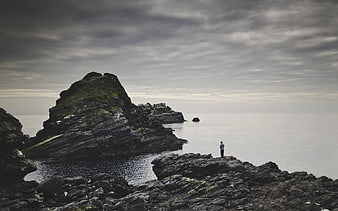 Lone Fisherman on Rocky Coastline Under Overcast Sky