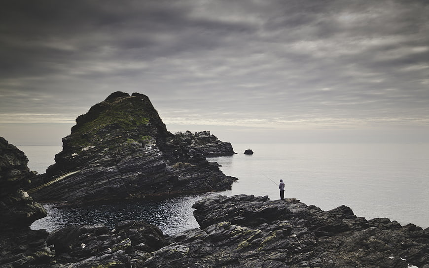 Lone Fisherman on Rocky Coastline Under Overcast Sky