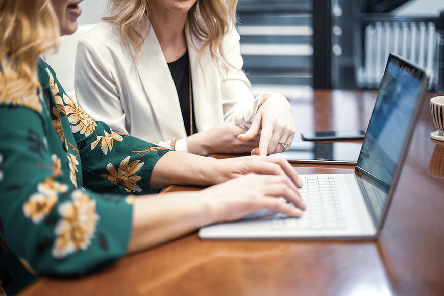 Two female colleagues collaborating on a laptop in a modern office