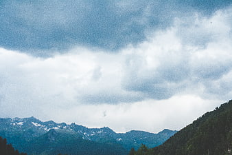 Dramatic cloudy sky over snow-capped mountain peaks and forest