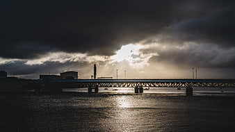 Dramatic Bridge Silhouette Over River with Sun Rays Through Clouds